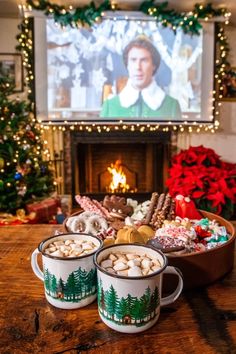 two mugs filled with hot chocolate and marshmallows in front of a fireplace