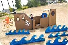 there is a cardboard boat with an anchor on it and other toys in the sand