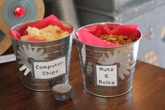 two metal buckets sitting on top of a table filled with chips and muffins