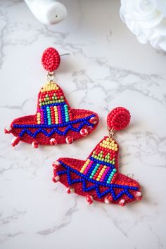 two red and blue beaded earrings sitting on top of a marble counter next to a white vase