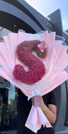 a woman holding a pink flower bouquet in front of a building with the number 3 on it