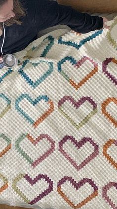 a woman laying on top of a bed next to a white blanket with colorful hearts