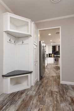 an empty kitchen with white cabinets and wood flooring in the hallway leading to the living room