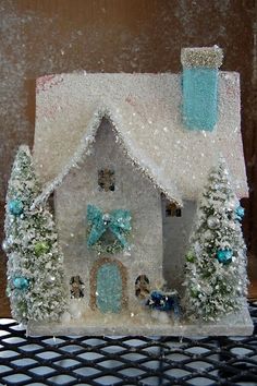 a small white house with snow on the roof and trees around it in front of a window