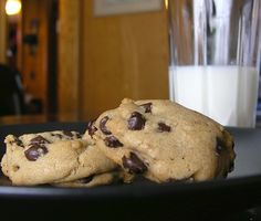 two chocolate chip cookies on a black plate with a glass of milk in the background