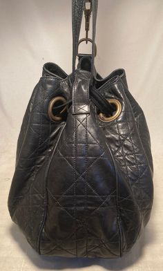 Christian Dior Black Leather Cannage Drawstring Shoulder Bag in very good condition. black cannage quilted leather trimmed with antiqued bronze hardware. Drawstring style top opens to a red nylon lined interior with one zip and 2 slit side pockets. Clean corners and exterior. Light pen marks/stains inside and one stripe of darkness above slit pockets see photos for details. Purchase includes dust cover. measurements: 15"x12"x6" 12" strap drop Drawstring Shoulder Bag, Bronze Hardware, Vuitton Bag, Quilted Leather, Dust Cover, Casual Backpack, Dior Bag, Womens Backpack, Antique Bronze