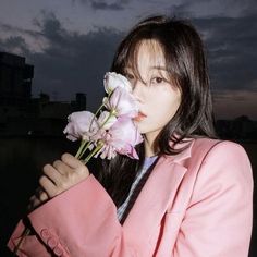 a woman in a pink coat holding flowers up to her face and looking at the camera