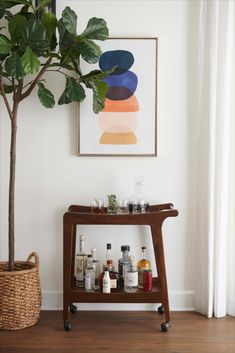 a wooden bar cart with liquor bottles on it next to a potted plant