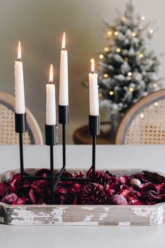 four candles are placed in a tray with red flowers