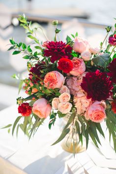 a vase filled with red and pink flowers on top of a white cloth covered table