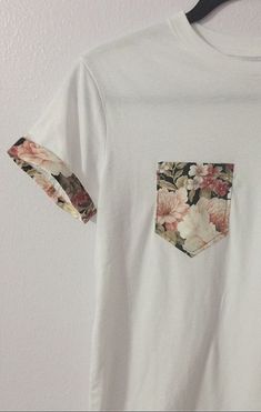 a white t - shirt with floral pocket on the front and back, hanging from a hanger