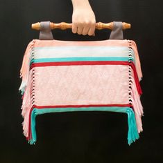 a hand holding a pink and blue bag with tassels on it's handles