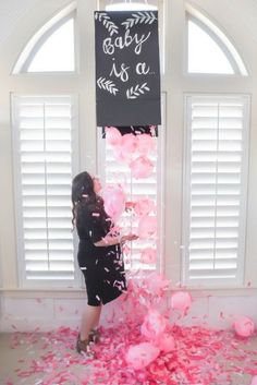 a woman standing in front of a window surrounded by pink balloons and confetti