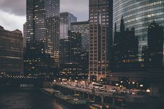 the city skyline is lit up at night, with skyscrapers and boats in the water