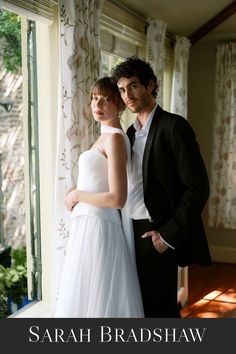 a man and woman standing next to each other in front of a window