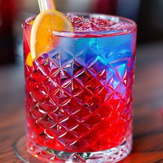 a red and blue drink sitting on top of a table next to a lemon wedge