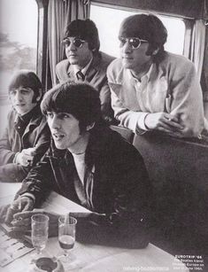 the beatles sitting at a table with drinks in front of them and looking off into the distance