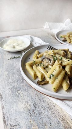 two plates of pasta with mushrooms and cheese on the table next to a bowl of sauce