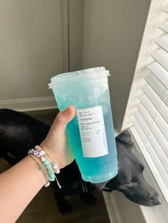 a person holding up a plastic cup in front of a black dog