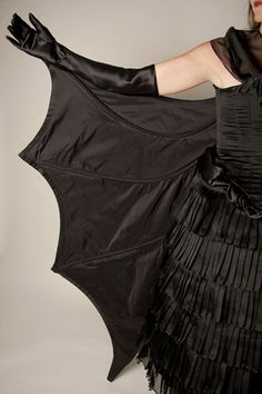 a woman in a black dress holding up a bat shaped object with fringes on it