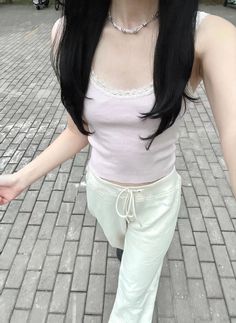 a woman with long black hair walking down a brick road wearing white pants and a pink tank top