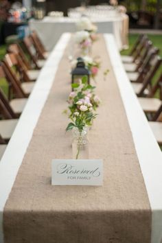 a long table is set up with flowers in vases and place cards on it