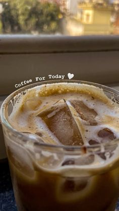 an iced drink in a glass on a table next to a window with the words coffee for today written above it