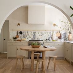 a kitchen with an archway leading into the dining room and kitchen area, along with a round wooden table surrounded by stools