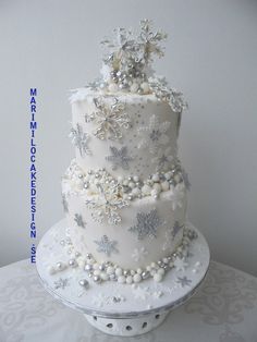 a three tiered white wedding cake with snowflakes and pearls