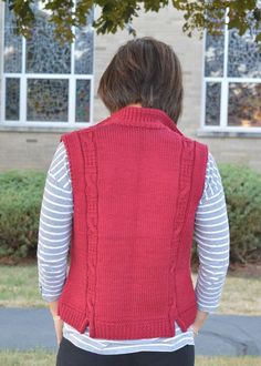 a woman standing in front of a building wearing a red sweater vest