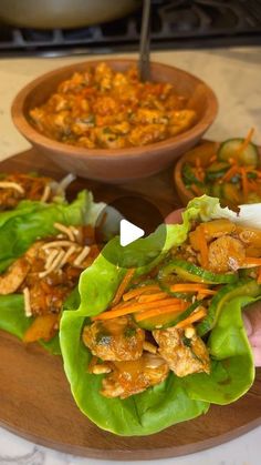 lettuce wraps filled with meat and vegetables on a cutting board next to a bowl of soup