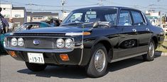 an old black car is parked on the side of the road in front of other cars