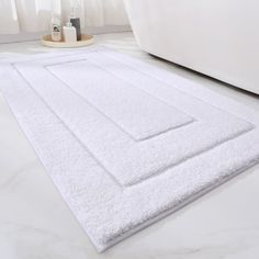 a white bath rug on the floor in a bathroom