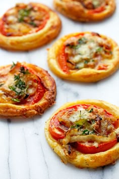 mini pizzas with cheese and tomatoes on them sitting on a marble counter top, ready to be eaten