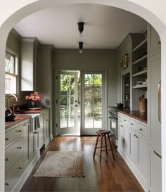 an archway leading into a kitchen with wooden floors and white cabinets, along with a rug on the floor