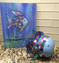 a fish made out of plastic beads sitting on top of a counter next to a book