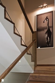 a giraffe standing next to a staircase in a house with white walls and wood handrails