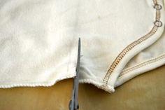 a pair of scissors cutting through the side of a piece of white fabric with gold thread