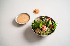 a salad in a bowl next to a small bowl of seasoning on a table