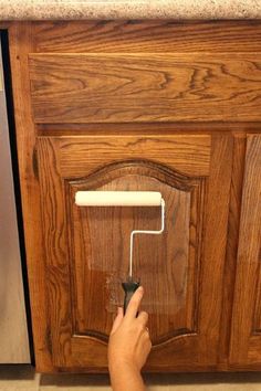 a person using a paint roller on the side of a kitchen cabinet with wood cabinets