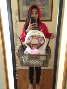 a woman taking a selfie in front of a mirror holding a basket filled with an ugly doll