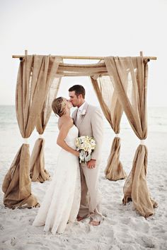 a bride and groom kissing on the beach in front of an open air gazebo