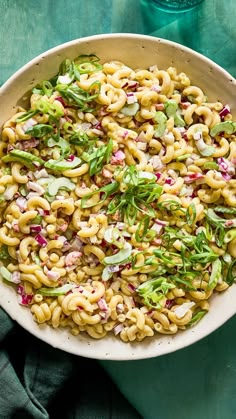 a bowl filled with pasta salad on top of a green table cloth next to a bottle of water