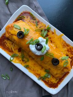 an enchilada dish with sour cream and black olives on the side