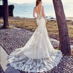 a woman in a wedding dress is standing by some trees and looking at the water