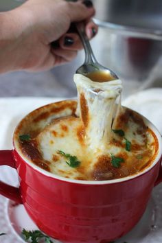 someone is dipping something into a cup of soup with a ladle in their hand