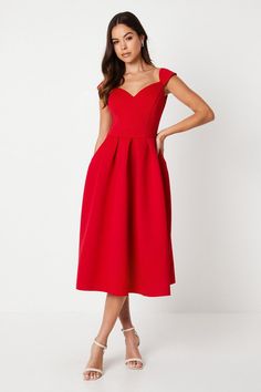 a woman is wearing a red dress with straps on the waist and shoulders, she has her hands on her hips