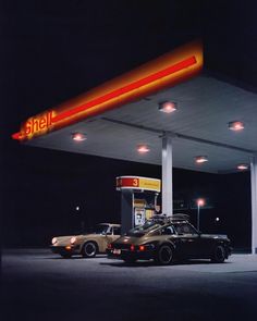 two cars are parked in front of a shell gas station at night with the lights on