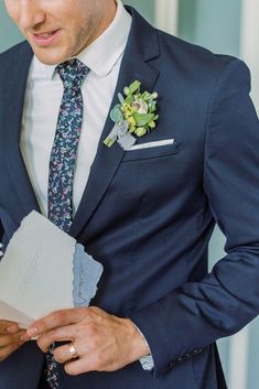 a man in a blue suit and flowered boutonniere holding a piece of paper