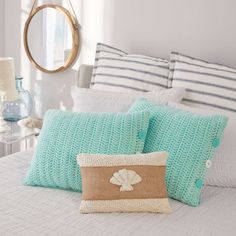 a white bed topped with lots of pillows next to a round mirror and table lamp